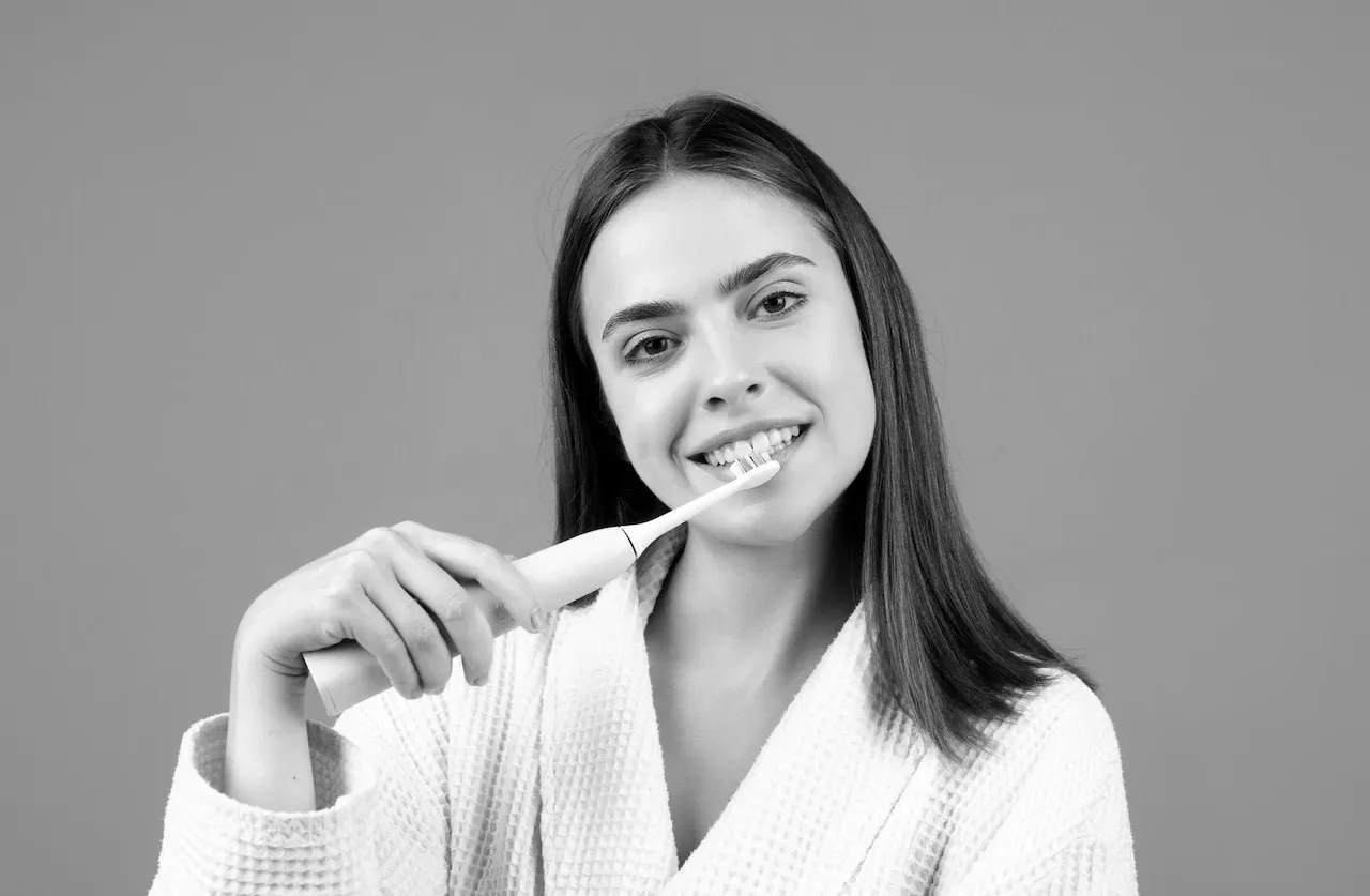 Persona cepillándose los dientes con un cepillo de cerdas suaves frente al espejo en una clínica dental moderna.